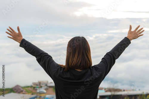 Young woman standing on a mountain with raised hands and looking to view of landscape