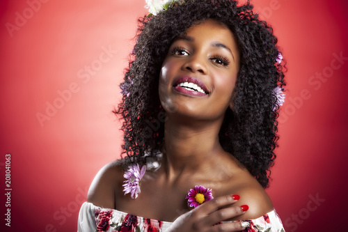 African american woman with curly black hair and flowers smiles while wearing pink lipstick. long beautiful eye lashes, great smooth skin.  makeup is flawless