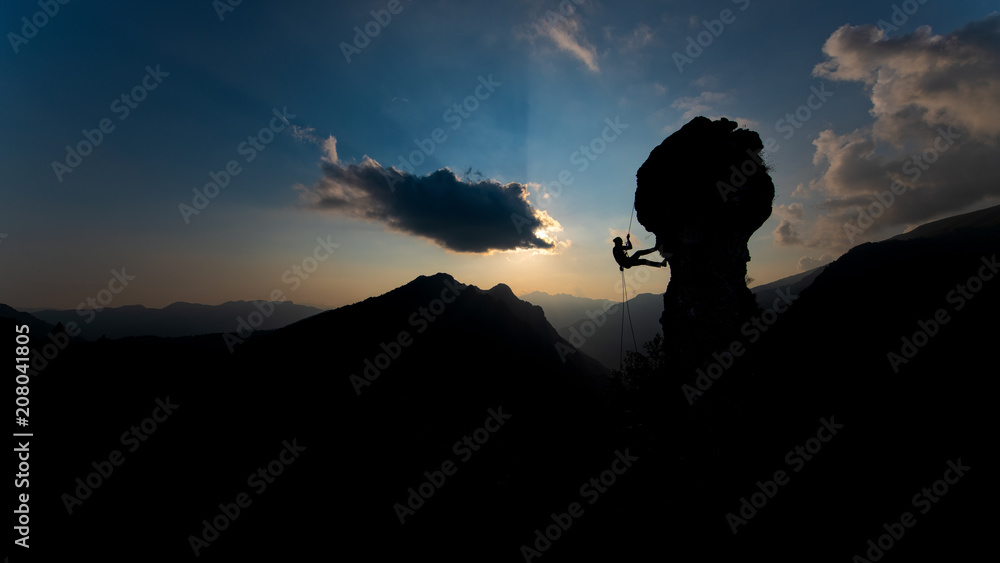Silhouette of a rock climber descending on the rope after climbing at sunset