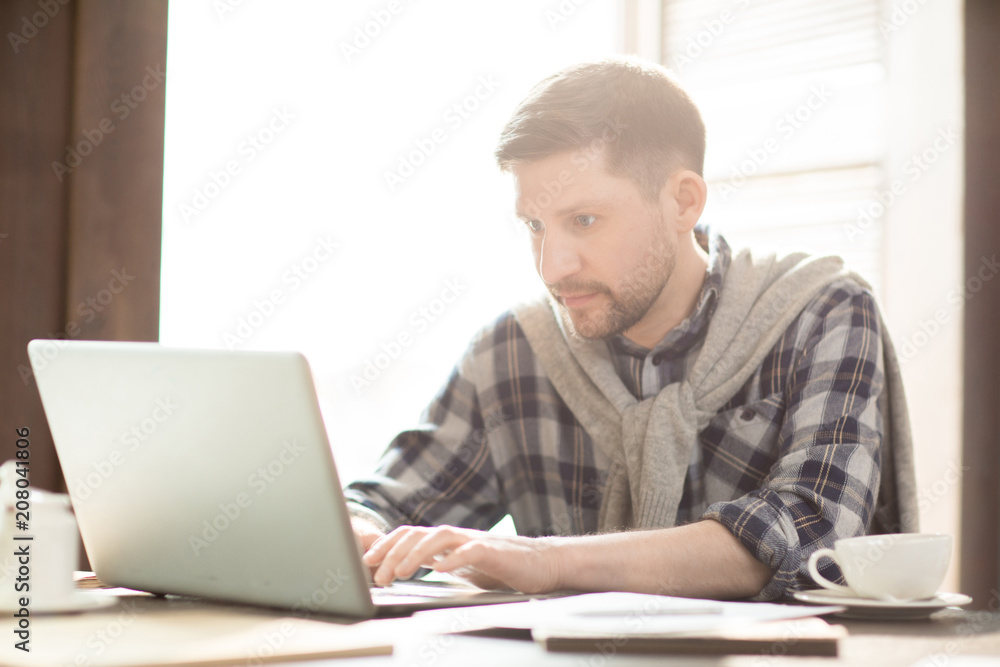 Handsome man in casual outfit sitting in cozy cafe and fulfilling business project with laptop. Handsome man in casual outfit sitting in cozy cafe and fulfilling business project with laptop.