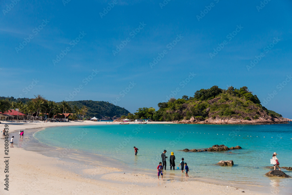 Tourists, adults and children are enjoying their leisure time at the beautiful white sandy Long Beach (Pasir Panjang) with its crystal clear turquoise blue water on Redang Island, Malaysia.