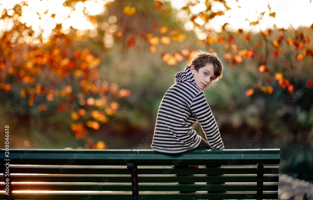 Boy perched on the back of a park bench in a park in autumn Stock Photo ...
