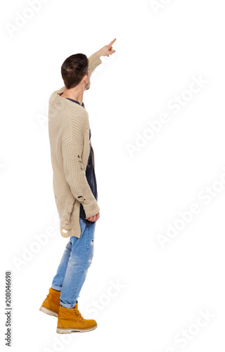 Back view of a stylish man in a knitted sweater points his hand upwards.