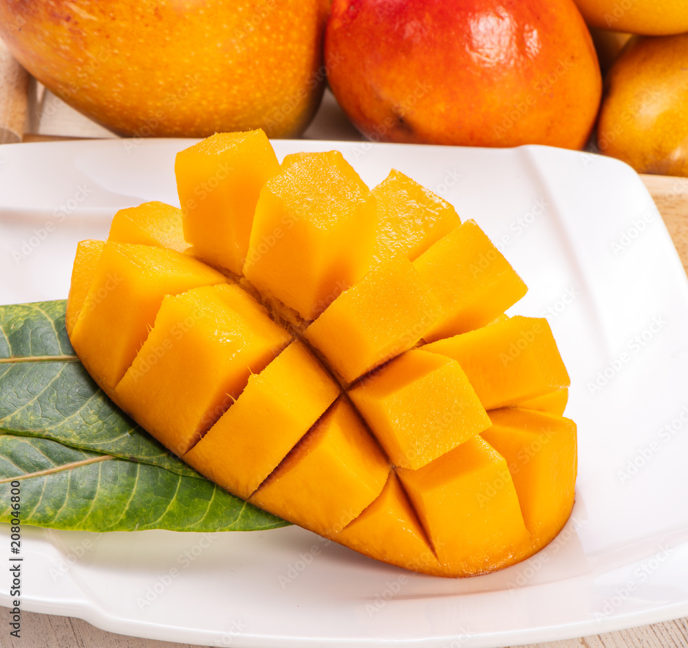 Fresh and beautiful mango in a white plate with sliced diced mango chunks isolated with light wooden background, copy space(text space), blank for text Fresh and beautiful mango in a white plate with sliced diced mango chunks isolated with light wooden background, copy space(text space), blank for text