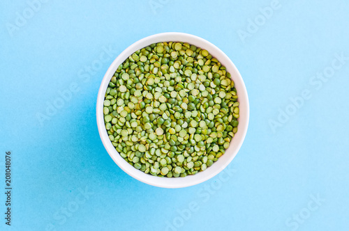 Raw uncooked green peas in a white bowl on a light blue background. Top view and copy space.