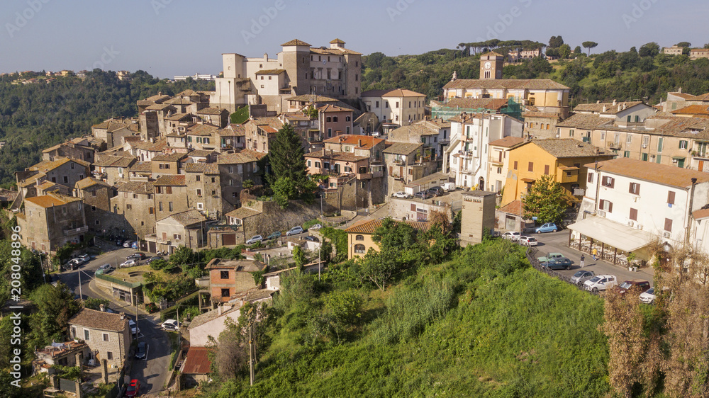 Aerial view of the village of Castelnuovo di Porto, near Rome, in Italy. The village is built perched on a hill and overlooks a green valley full of trees. At the top there is the medieval castle.