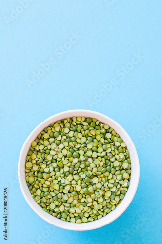 Raw uncooked green peas in a white bowl on a light blue background. Top view and copy space.