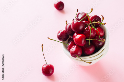 Heap of fresh ripe red cherries in a white bowl on a pink background. Top view and copy space. Organic food concept.