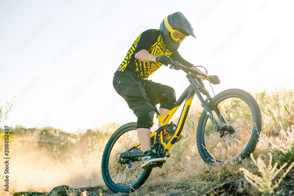 Naklejka premium Cyclist Riding the Mountain Bike on the Summer Rocky Trail at the Evening. Extreme Sport and Enduro Cycling Concept.