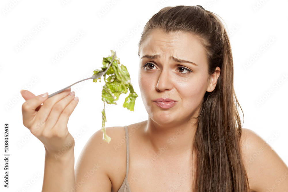 Young unhappy woman holding fork with lettuce on white background Young unhappy woman holding fork with lettuce on white background