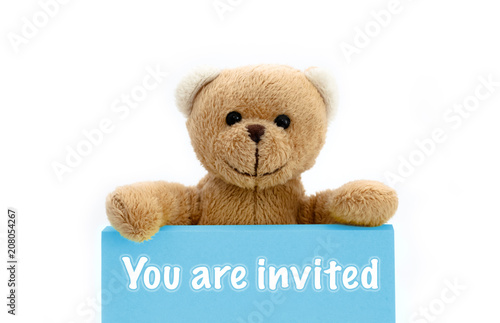 You are invited blue card with brown teddy bear holding with the two hands the note with the message. Photo isolated in a seamless white background. © fewerton