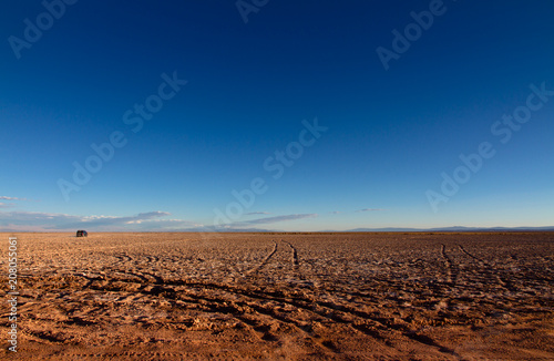 Panoramic landscape view near    Ojos del Salar    in the Atacama Desert  Chile  depicting tire tracks contrasting the wilderness and immense dimensions of the desert with a mountain chain in the distant.