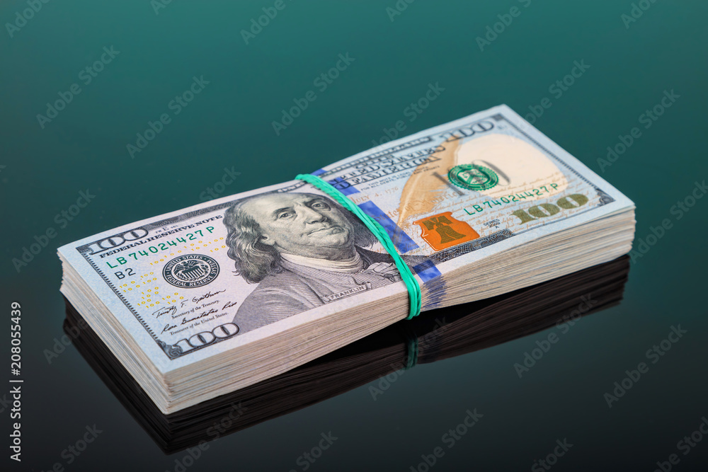 pack of 100 $ banknotes tied with an elastic band lies on a dark mirror surface pack of 100 $ banknotes tied with an elastic band lies on a dark mirror surface