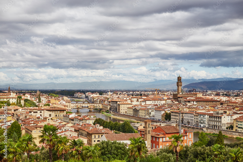 Picturesque view of Florence city with colorful old buildings under dark clouds, Italy