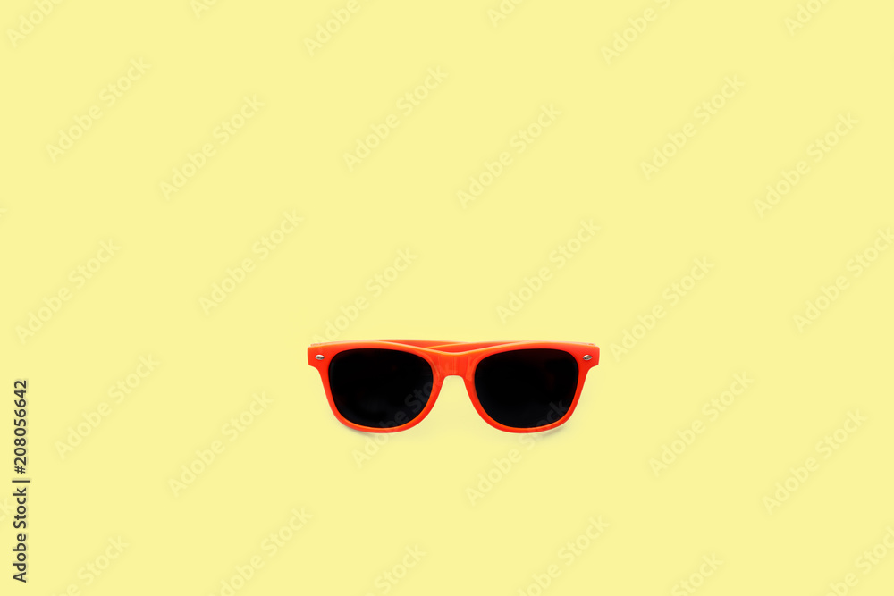 Summer orange sunglasses isolated in large pastel yellow background. Minimal concept image for sun protection, hot days, tropical travel, summer vacations and beach holidays.