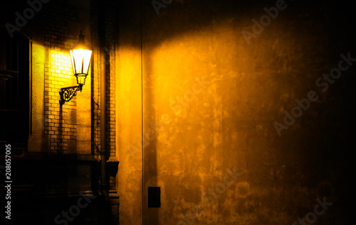 Old lantern illuminating a dark alleyway corner wall at night in Prague  Czech Republic. Photo almost monochromatic with brown yellow tones from the lantern as light source against the dark shadows