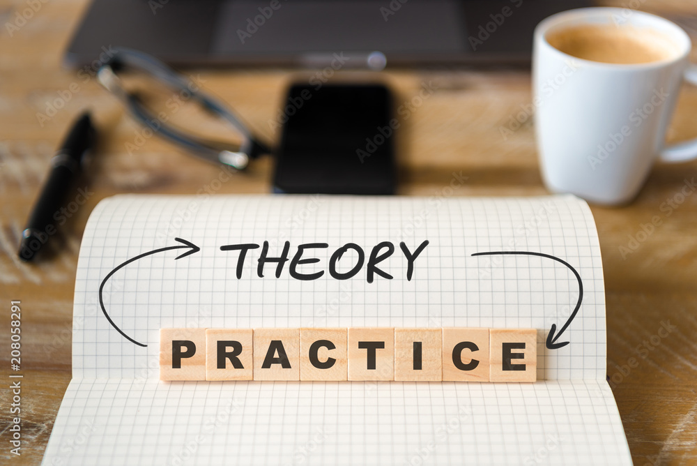 Closeup on notebook over wood table background, focus on wooden blocks with letters making Theory into Practice text