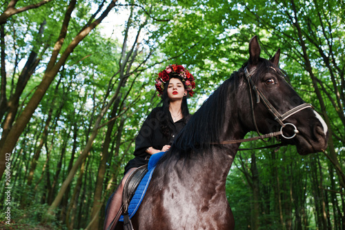 Mystical girl in wreath wear in black at horse in wood. © AS Photo Family