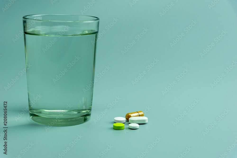 various pills and glass of water on gray background various pills and glass of water on gray background