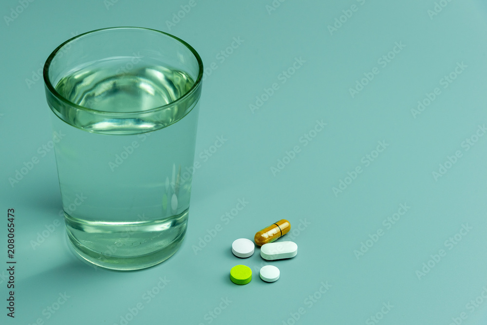 various pills and glass of water on gray background various pills and glass of water on gray background