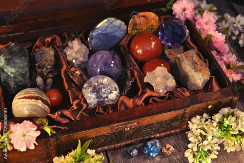 Close up of box with magic crystals and stones, sakura spring flowers on planks. Occult, esoteric and divination still life. Halloween background with vintage objects