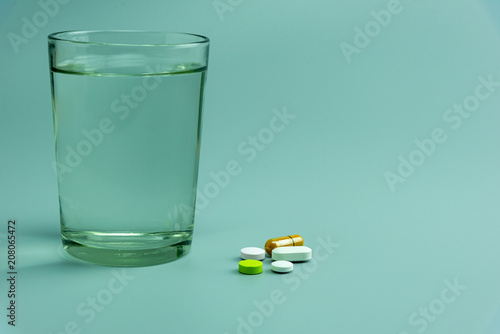  various pills and glass of water on gray background