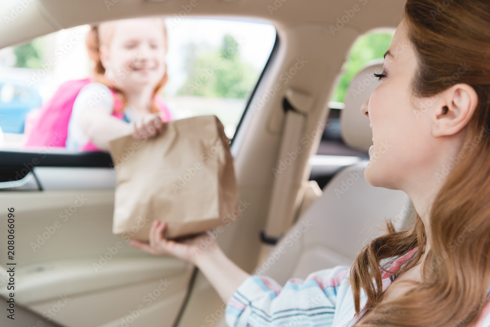selective focus of mother in car giving paper package with food to daughter