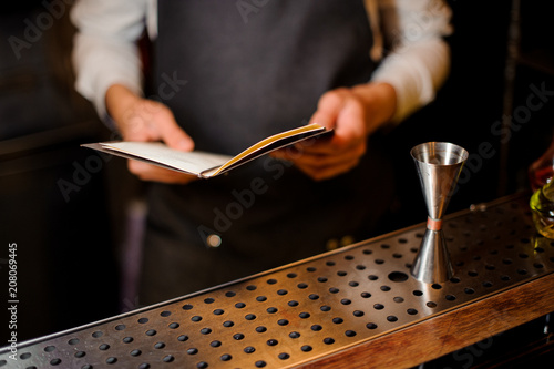 Bartender standing at the bar counter with a recipe book