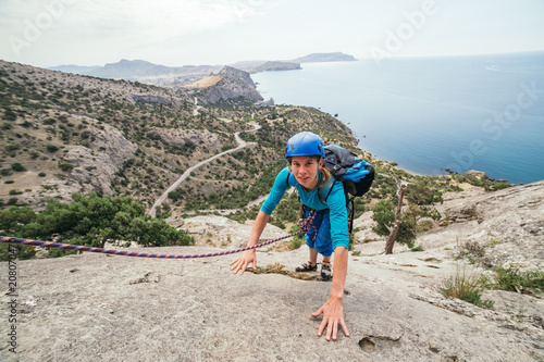 A girl in a special equipment and helmet climbs mountain pitch near the sea cost