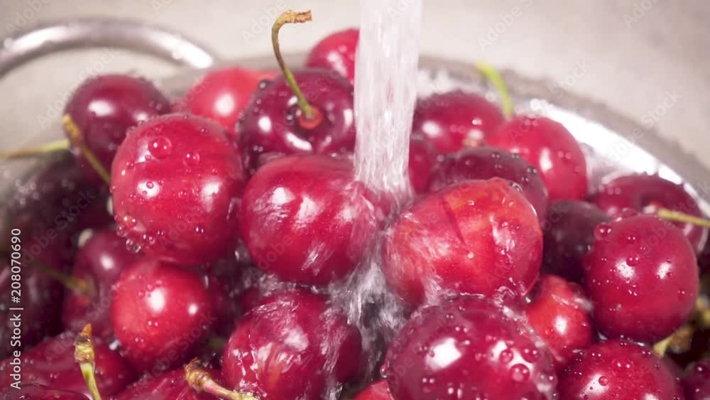 Slow motion the camera moves on a beautiful sweet cherry in a metal colander in a sink under a stream of water Slow motion the camera moves on a beautiful sweet cherry in a metal colander in a sink under a stream of water
