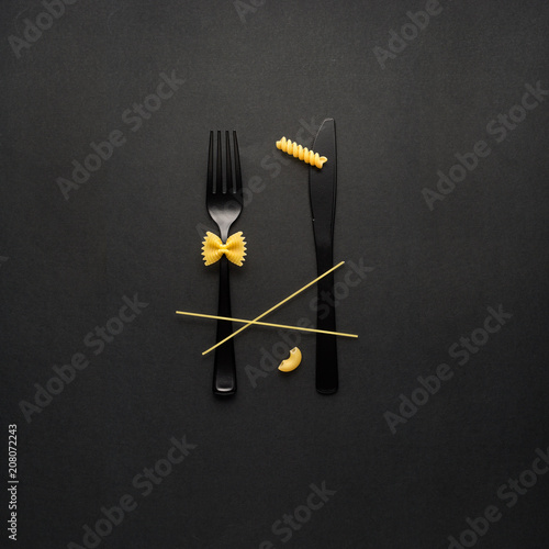 Tasty pasta / Creative still life photo of fork and spoon with raw pasta on black background.