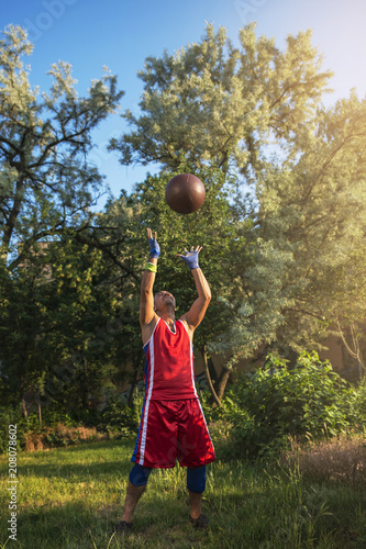 Young athlete performs sports exercises with a ball outdoors. © igorgeiger