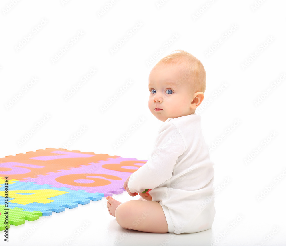 The baby is sitting on the floor near the developing color Mat. The baby is sitting on the floor near the developing color Mat.