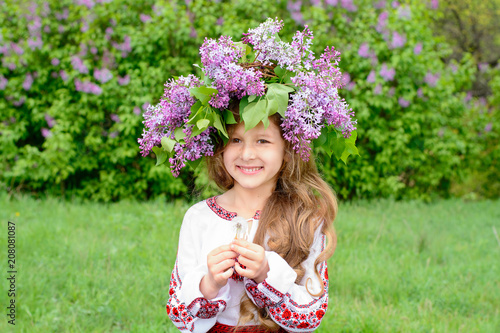 a beautiful girl in a wreath is wearing an embroidery. smiling and holding a dandelion