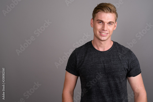 Young handsome man with blond hair wearing gray shirt against gr