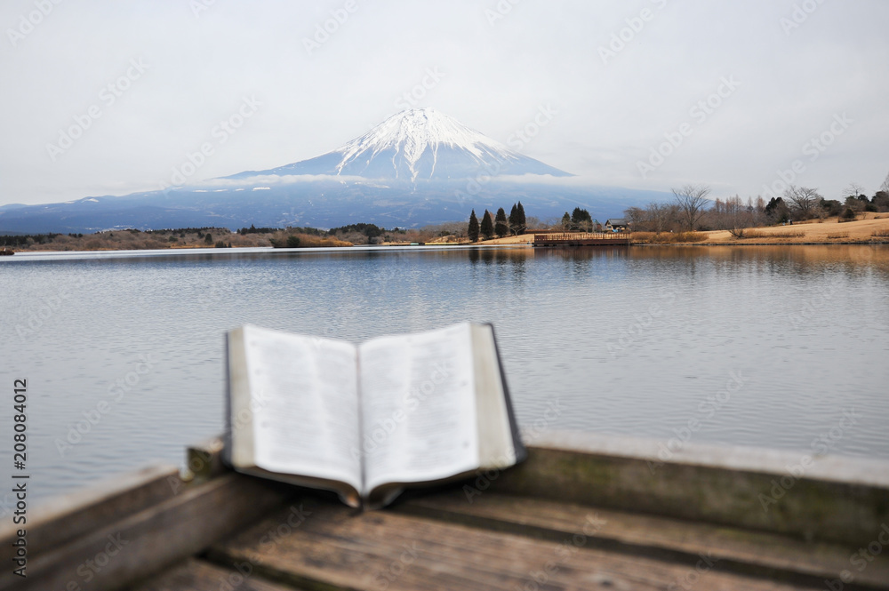 Bible open on a wooden bridge in front of the beautiful Mount Fuji on a cold and cloudy afternoon. Tanuki lake, Japan.