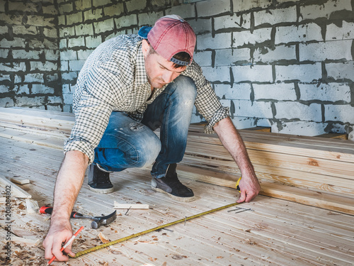 Stylish guy in a baseball cap, jeans and a shirt, working with tools on wood inside the house under construction. Concept of construction and repair