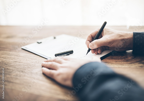 close-up shot of businessman signing contract or document on wooden desk photo