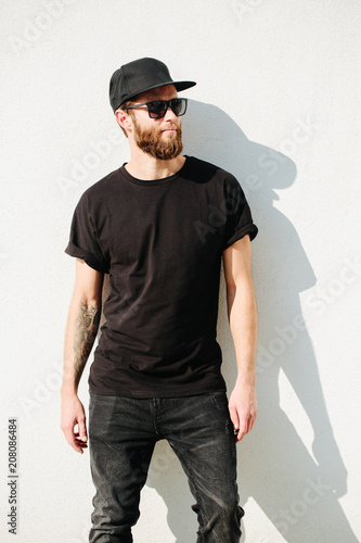 Hipster handsome male model with beard wearing black blank t-shirt with space for your logo or design in casual urban style