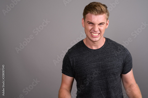 Young handsome man with blond hair wearing gray shirt against gr