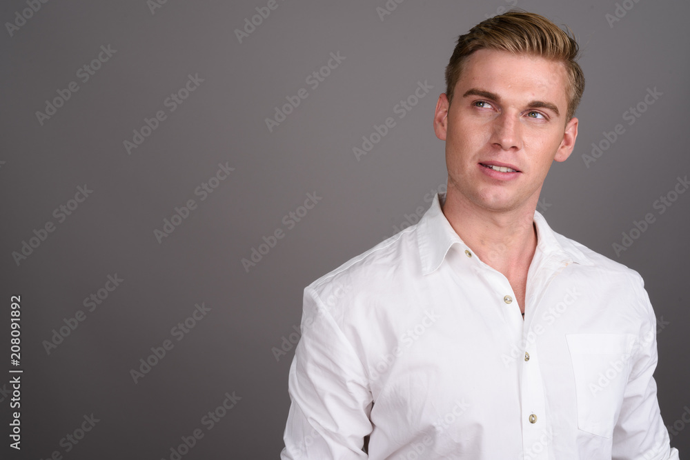 Young handsome businessman with blond hair against gray backgrou Young handsome businessman with blond hair against gray backgrou