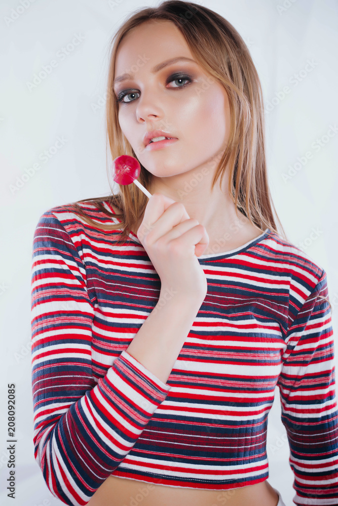 Young glamour sexy girl with lollipop looking at the camera.Sexual young blonde woman portrait with bright makeup looking forward holding and licking round red sugar candy Young glamour sexy girl with lollipop looking at the camera.Sexual young blonde woman portrait with bright makeup looking forward holding and licking round red sugar candy