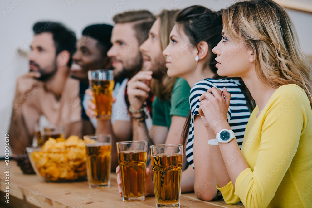 side view of group of multicultural friends drinking beer and watching soccer match at bar side view of group of multicultural friends drinking beer and watching soccer match at bar