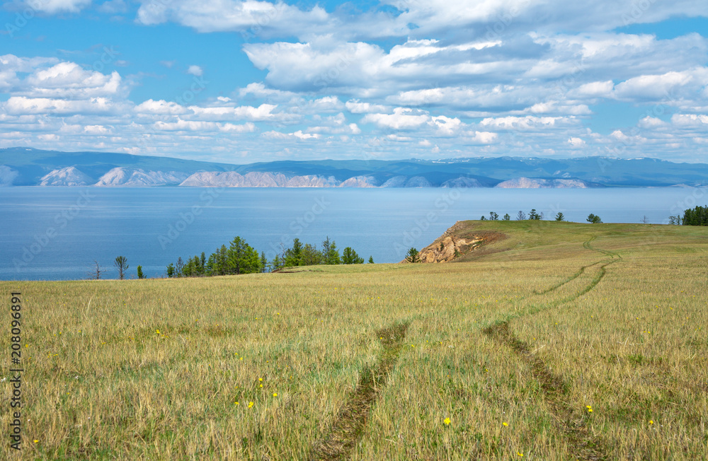 Baikal Lake on sunny June day. View from the Olkhon Island to the Maloye More Strait. The road to the shore along the steppe field
