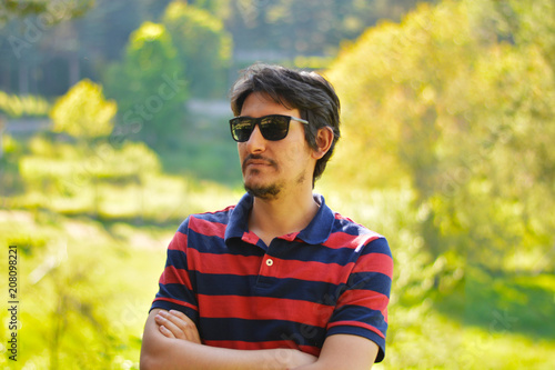 Young man outdoors portrait looking at the camera with natural green background. Neutral Facial Emotion.