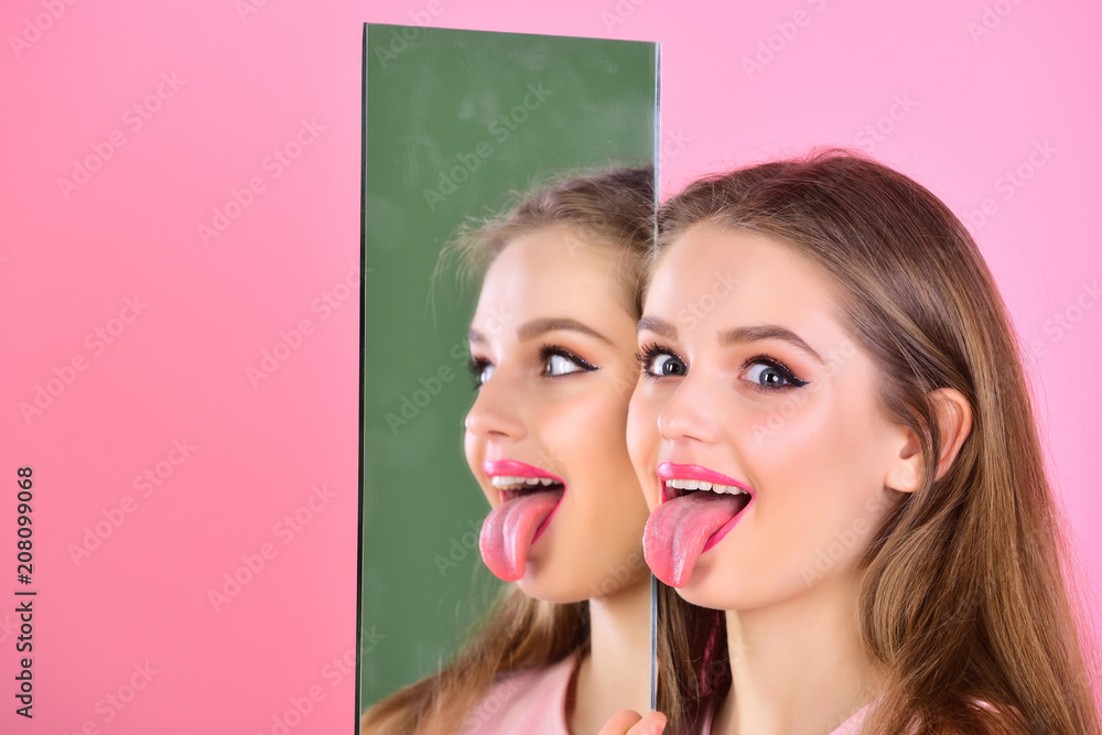 Girl show tongue at mirror as multifaceted personality. Beauty and Hairdresser salon and makeup concept. Healthy teeth and skincare of happy girl. Sensual lady with long hair pretty face Stock