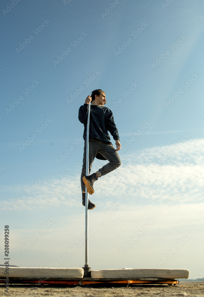 a sporty man in a black keeps his hand at pole on the background of blue sky. a sporty man in a black keeps his hand at pole on the background of blue sky.