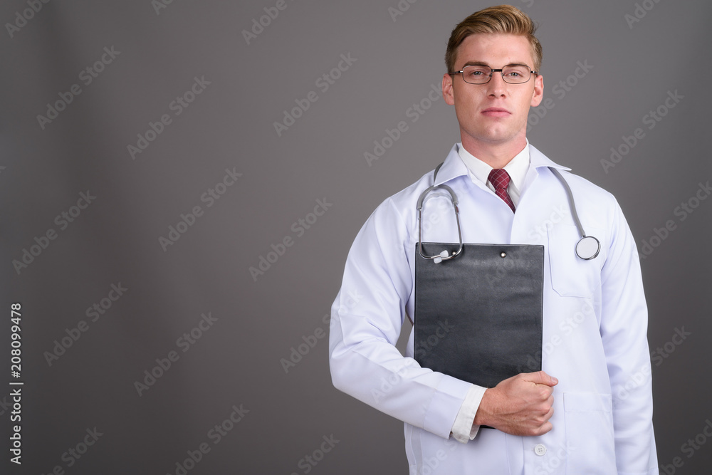 Young handsome man doctor with blond hair against gray backgroun Young handsome man doctor with blond hair against gray backgroun