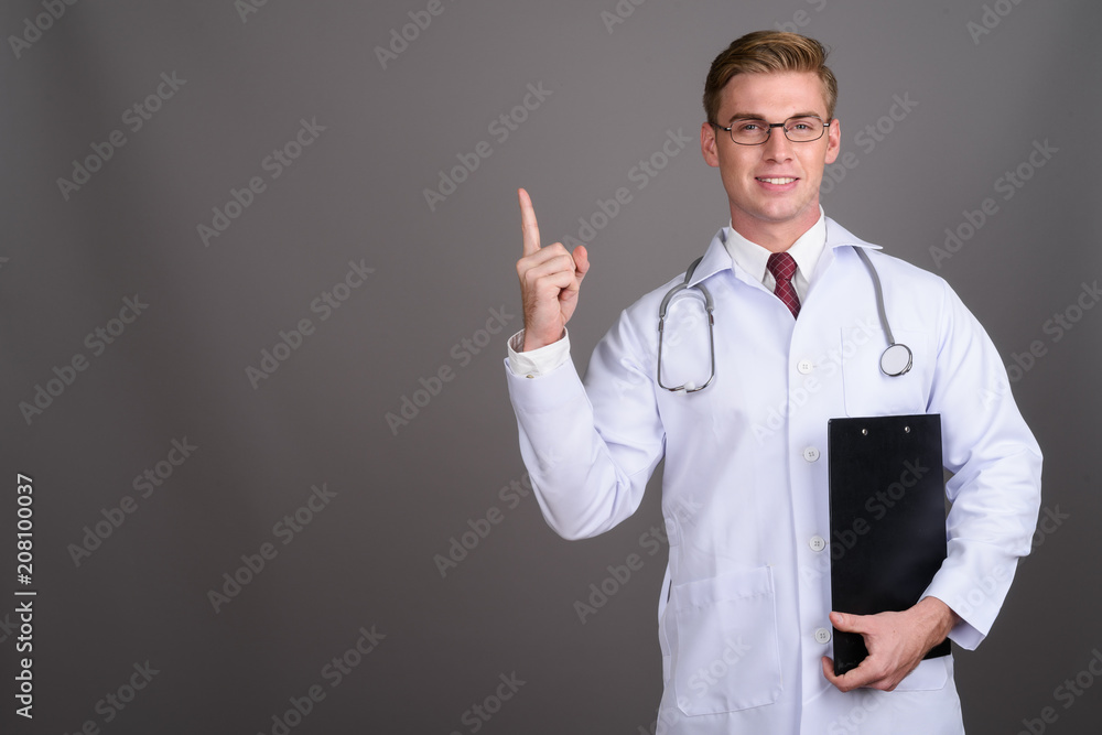 Young handsome man doctor with blond hair against gray backgroun Young handsome man doctor with blond hair against gray backgroun