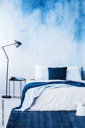 Navy blue carpet in front of bed next to lamp in bedroom interior with wallpaper